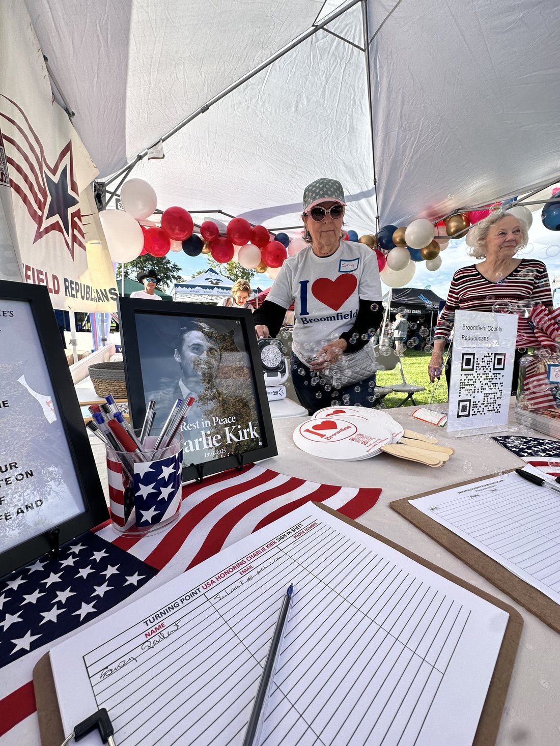 BCRC volunteers staffing the booth at Broomfield Days, with a memorial photo of Charlie Kirk on the table